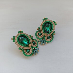 May include: A pair of green and gold earrings with a teardrop-shaped green gemstone in the center of each earring.