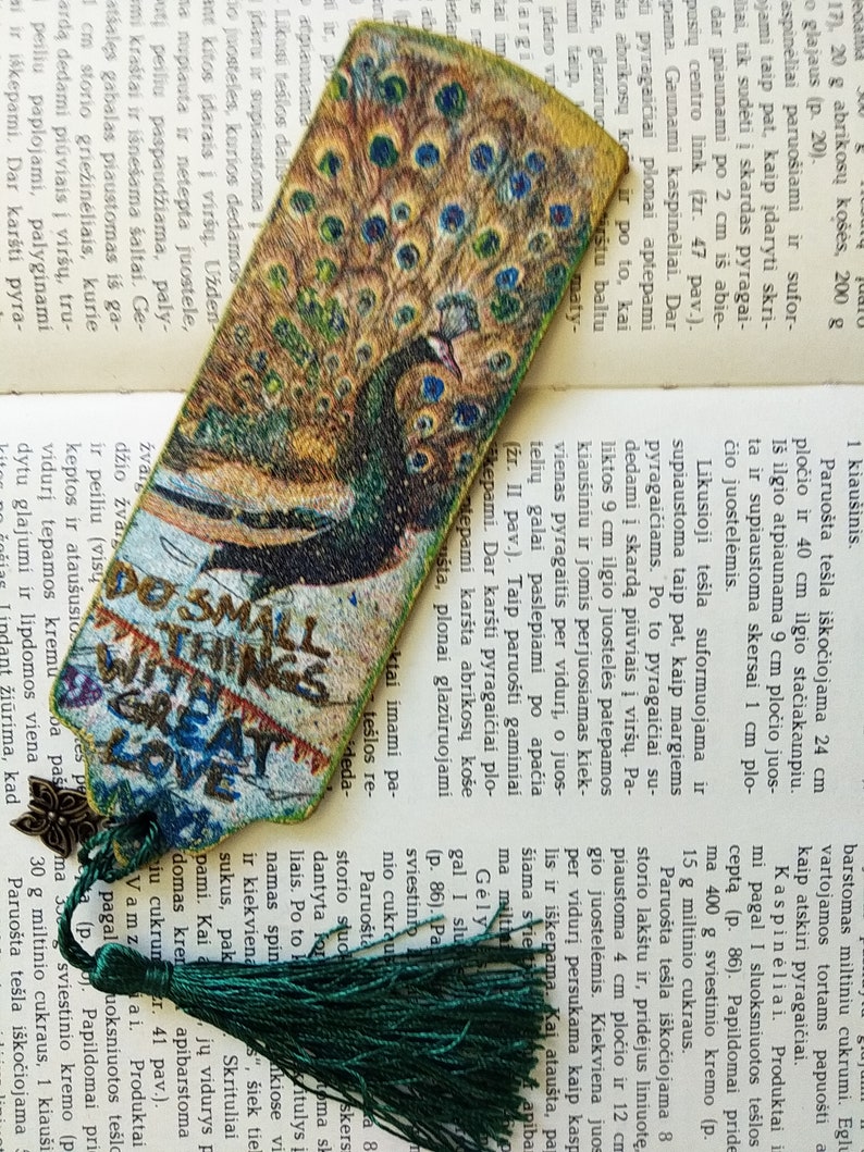 May include: A green and gold peacock bookmark with a green tassel. The bookmark has the text "Do small things with great love" printed on it.