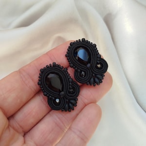 Könnte beinhalten: Ein Paar schwarze Ohrringe mit einem großen, tropfenförmigen schwarzen Edelstein in der Mitte. Die Ohrringe sind von aufwendigen schwarzen Perlen umgeben, vor weißem Hintergrund.