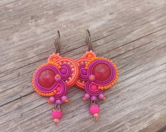 May include: A pair of pink and orange earrings with a large pink stone in the center of each earring. The earrings are made of polymer clay and have a delicate, intricate design.