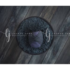 May include: A dark gray, fluffy, circular backdrop with a purple and gray fabric prop in the center. The backdrop is on a dark wood surface.