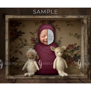 May include: A newborn baby wrapped in a burgundy swaddle is lying in a vintage wooden box with a floral wallpaper background. The baby's face is covered with a transparent overlay that says "Put your face here". Two stuffed animals, a white lamb and a brown deer, are sitting next to the baby.