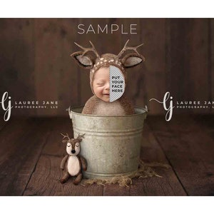 May include: A newborn baby wearing a brown deer costume is sitting in a metal bucket. The baby is smiling and has a deer headband on. There is a small stuffed deer toy in front of the bucket. The background is a wooden wall.