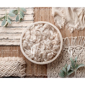 Puede incluir: Un cuenco blanco redondo lleno de material blanco y esponjoso, rodeado de varias telas texturizadas beige y crema, incluyendo una alfombra tejida, una manta con flecos y una pieza de macramé. Ramitas de vegetación están dispersas por toda la disposición.