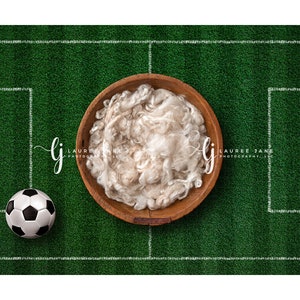 Puede incluir: Un nido de bebé de piel sintética blanca en un cuenco de madera sobre un campo de fútbol artificial verde con líneas blancas. Un balón de fútbol blanco y negro está en la esquina inferior izquierda de la imagen.