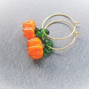 May include: Gold hoop earrings with orange pumpkin-shaped glass beads and green glass beads.