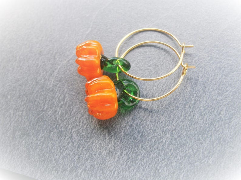 May include: Gold hoop earrings with orange pumpkin-shaped glass beads and green glass beads.