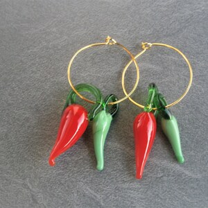 May include: A pair of gold hoop earrings with red and green glass chili pepper charms. The charms are detailed with green stems and leaves.