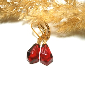 May include: A pair of gold earrings with red teardrop-shaped glass stones.