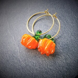 May include: Gold hoop earrings with orange and green glass pumpkin charms.