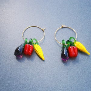 Vergoldete Creolen mit Gemüseanhängern (Aubergine, Paprika und Maiskolben) aus Lampwork Glas. Die Creolen sind aus vergoldetem Edelstahl. Die Aubergine ist violett, die Paprika rot und der Maiskolben gelb. Alle Anhänger haben einen grünen Stängel
