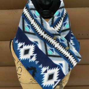 May include: A blue, white, and black fleece neck warmer with a geometric pattern. The neck warmer has two brown buttons on the side.