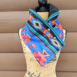 May include: A blue and black fleece neck warmer with a Southwestern-inspired geometric pattern. The warmer has two snap buttons on the side.