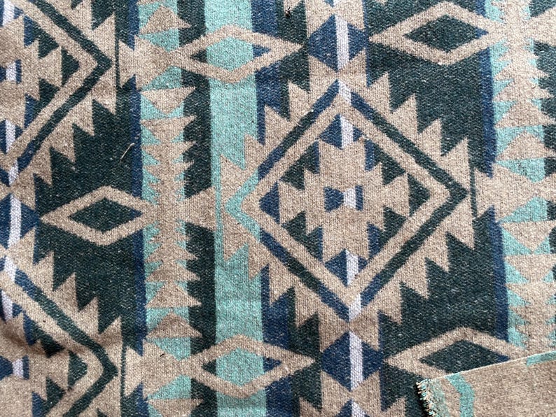 Pu&ograve; includere: Primo piano di un tessuto intrecciato con un motivo geometrico. Il design presenta forme ripetute a diamante e triangolari in tonalit&agrave; di verde acqua, blu navy e beige. Il tessuto ha un aspetto strutturato, che suggerisce una coperta o un tappeto.