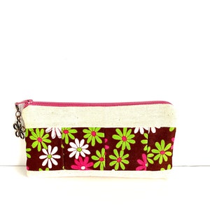May include: A small, brown and white floral print zippered pouch with a pink zipper and a silver charm.