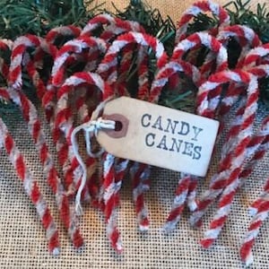 May include: A bunch of red and white candy canes made of pipe cleaners. The candy canes are arranged in a circle on a burlap background. A small tag with the words "CANDY CANES" is in the center of the circle.
