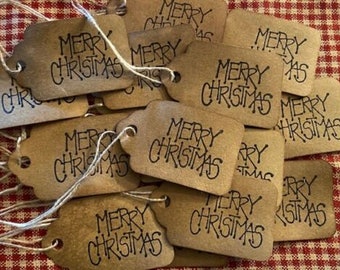 Puede incluir: Un conjunto de etiquetas de regalo de papel marrón con el texto "Merry Christmas" escrito en tinta negra. Las etiquetas están atadas con hilo y están listas para ser usadas para envolver regalos.