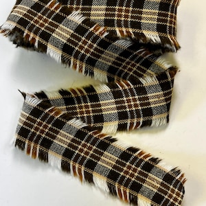 May include: Brown and white plaid ribbon with frayed edges. The ribbon features a classic plaid pattern in shades of brown and white, with a touch of beige. The frayed edges add a rustic, textured look. This ribbon is suitable for crafts and decorations.