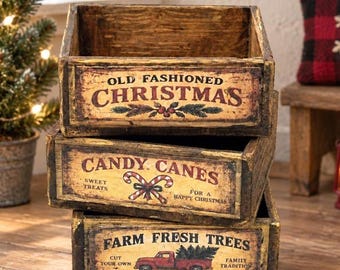 Könnte beinhalten: Ein Stapel aus drei rechteckigen Holzkisten mit abgenutzter Oberfläche. Die oberste Kiste trägt die Aufschrift OLD FASHIONED CHRISTMAS mit Stechpalmen. Die mittlere Kiste zeigt CANDY CANES SWEET TREATS FOR A HAPPY CHRISTMAS.
