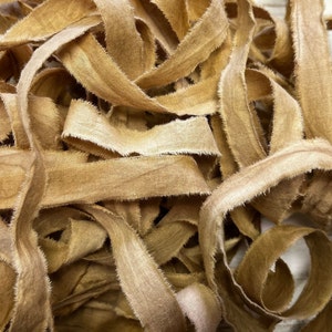 May include: A pile of frayed, tan fabric ribbon. The ribbon is woven and has a rough, textured surface.