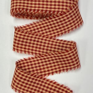 May include: Red and tan gingham ribbon with frayed edges. The ribbon is woven with a checkered pattern.