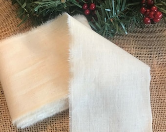 May include: Two pieces of off-white fabric, one folded and one flat, with a slightly rough texture. The fabric is lying on a brown burlap surface.