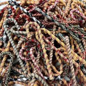 May include: A pile of fabric candy canes in various plaid patterns, including red, green, black, and white. The candy canes are made from repurposed fabric and are perfect for adding a touch of rustic charm to your holiday decor.