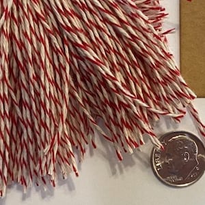 May include: A close-up of a bundle of red and white baker's twine. The twine is approximately 1/2 inch in diameter and is shown next to a US dime for scale.
