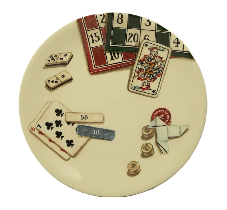 K&ouml;nnte beinhalten: Ein cremefarbener dekorativer Teller mit Illustrationen von Spielkarten, Dominosteinen und Spielbrettern. Der Teller enth&auml;lt eine Spielkarte mit einem Narren, Bingokarten und Pokerchips. Das Design hat eine Vintage-&Auml;sthetik, handgemalt.