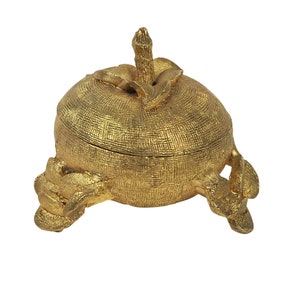 May include: A gold-colored metal trinket box shaped like a fruit with a textured surface. The box has three legs and a lid with a stem on top.