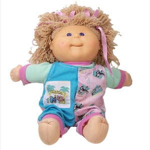 Pode incluir: Uma boneca Cabbage Patch Kid com cabelo loiro encaracolado vestindo uma roupa azul e rosa com estampa de animais da selva. A boneca tem olhos azuis e uma tez rosada.