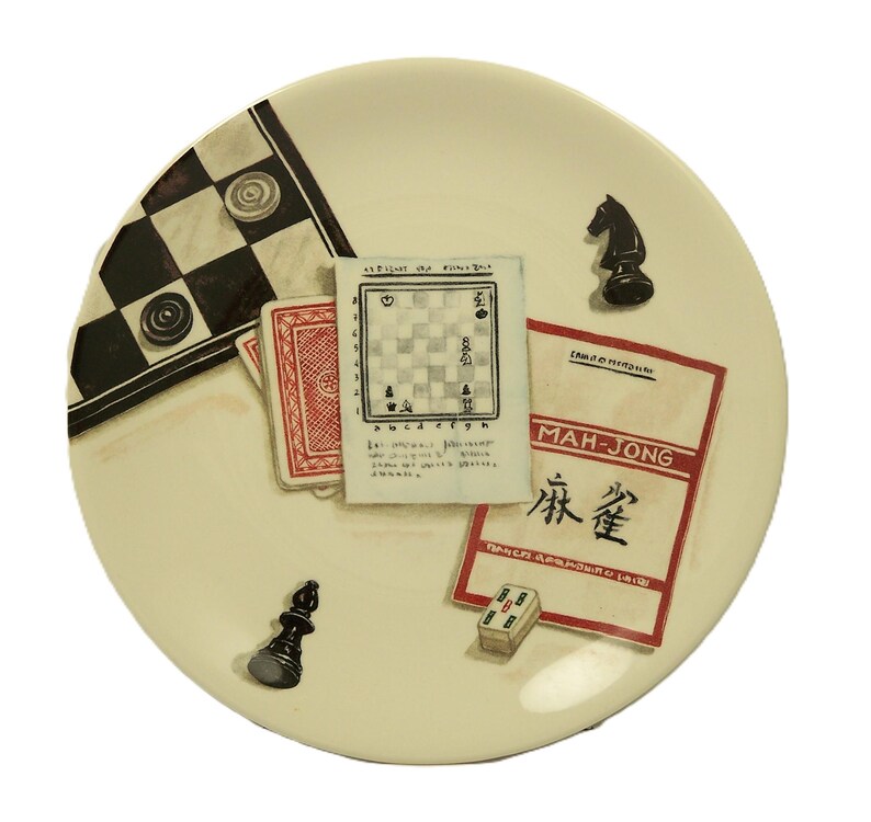 K&ouml;nnte beinhalten: Ein cremefarbener dekorativer Teller mit Illustrationen von Spielen. Der Teller zeigt ein Schachbrett, Spielkarten, ein Schachbrett, eine Schachfigur, einen Mah-Jongg-Stein und eine Mah-Jongg-Spielkarte.