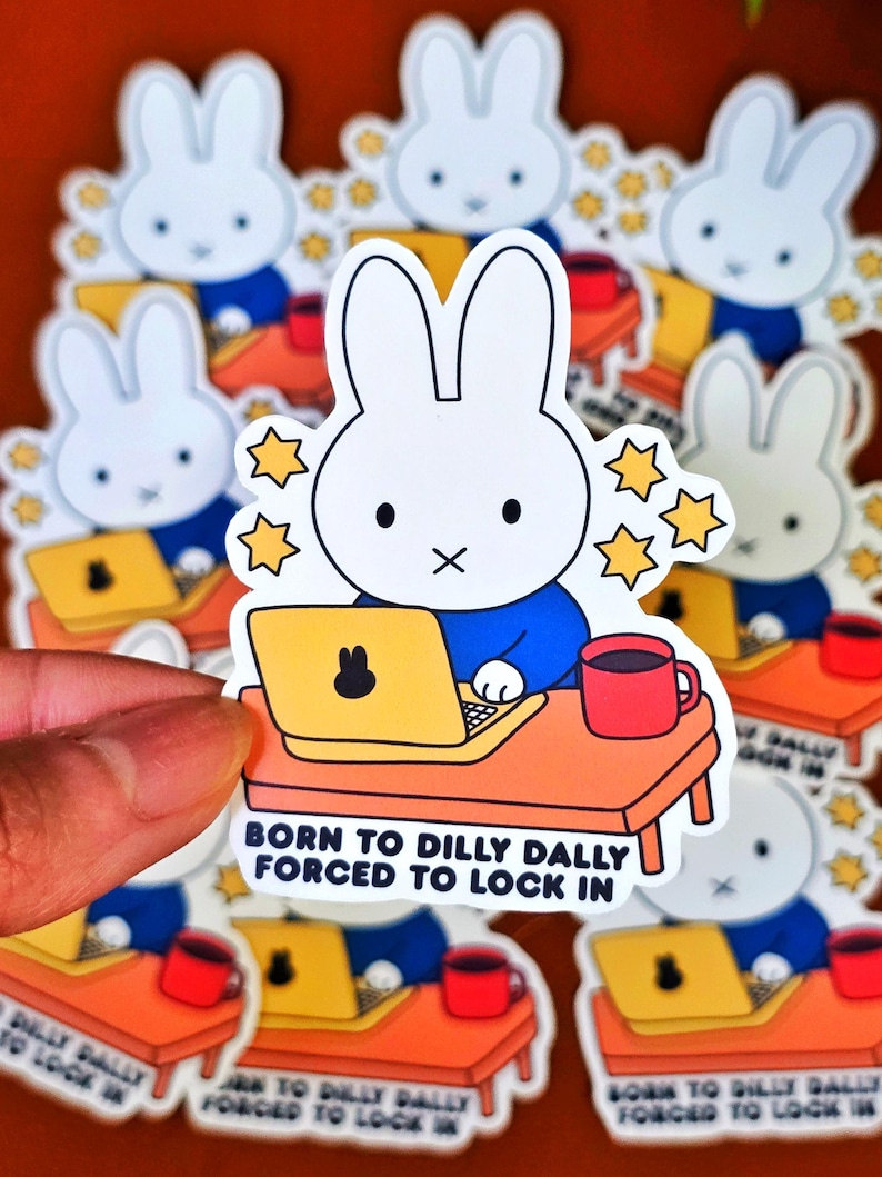 May include: A collection of stickers featuring a white bunny character with a blue shirt, working on a yellow laptop at an orange desk. The stickers have the text "BORN TO DILLY DALLY FORCED TO LOCK IN" and yellow star accents. A red mug is also on the desk.