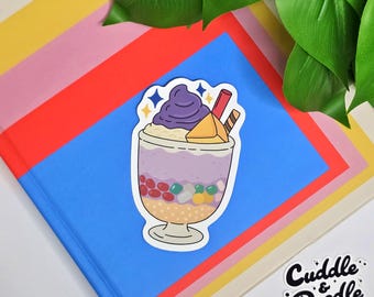 May include: A sticker of a purple and yellow dessert with a swirl of purple on top, surrounded by a white border. The sticker is on a blue and red background with the text "Cuddle & Doodle" in white on a black background.