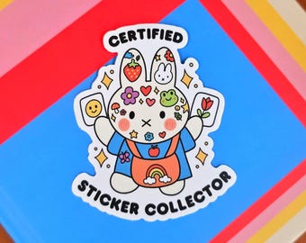 May include: A colorful sticker featuring a cartoon bunny with the text "CERTIFIED STICKER COLLECTOR". The bunny is wearing a blue outfit with an orange apron and holding cards with a smiley face and a flower. The sticker is decorated with various cute icons.