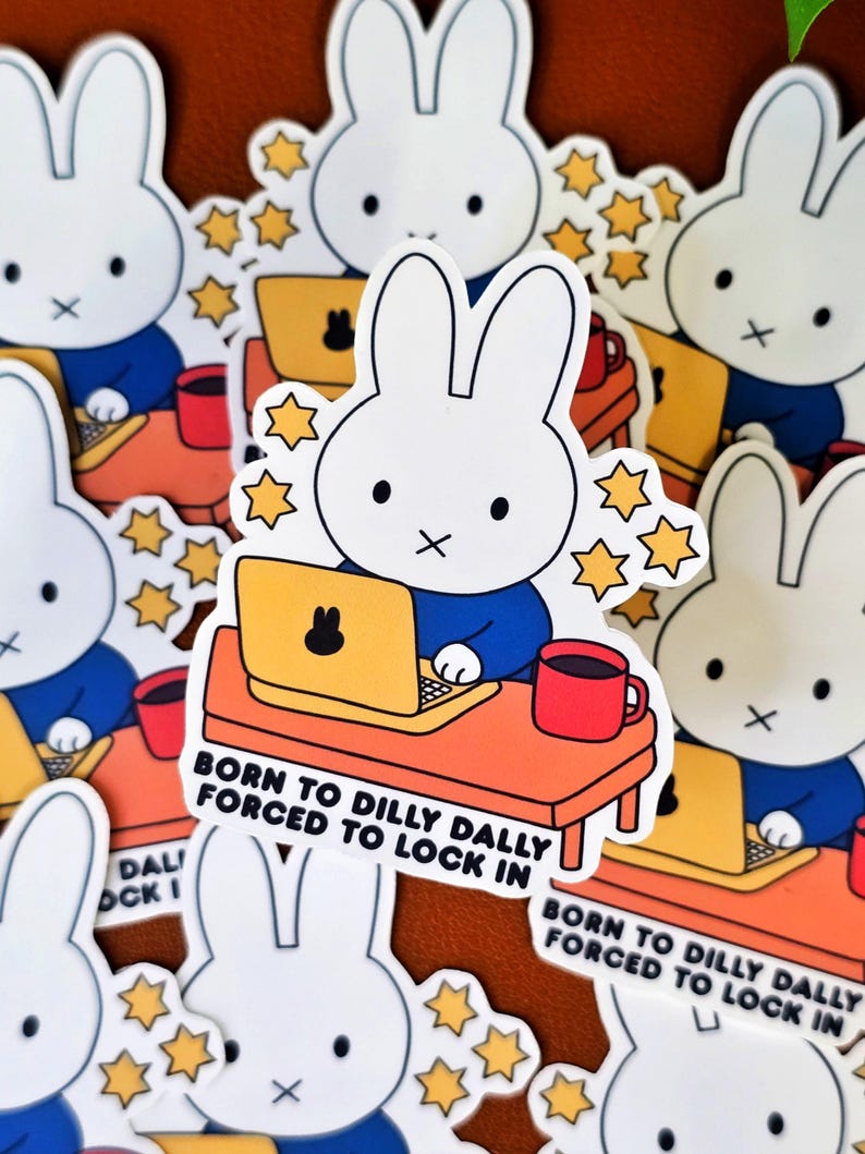 May include: White bunny stickers with a blue shirt, working on a yellow laptop at an orange desk, with a red mug. Text reads "BORN TO DILLY DALLY FORCED TO LOCK IN". Decorative star accents surround the bunny.
