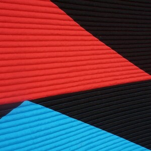 May include: A quilted wall hanging featuring three geometric shapes. The top shape is a large red triangle, the middle shape is a black triangle, and the bottom shape is a blue triangle.
