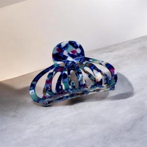 May include: A large, patterned hair claw clip in shades of blue, white, and purple. The clip has a rounded top and a series of curved, open sections. The claw clip is made of a glossy, marbled material.