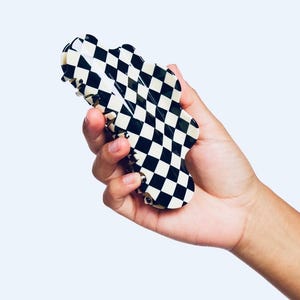 Puede incluir: Una pinza para el pelo a cuadros en blanco y negro. La pinza tiene forma de onda y un acabado brillante.