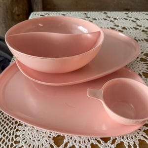 May include: A set of pink plastic divided serving dishes. The set includes a large oval platter, a smaller oval platter, a divided bowl, and a small cup.