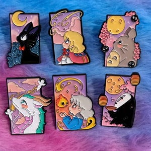 May include: Set of six enamel pins featuring characters from animated films. Each pin has a rectangular shape with a black outline and depicts a different character against a colorful background. The pins include a black cat, a girl, and a gray creature.
