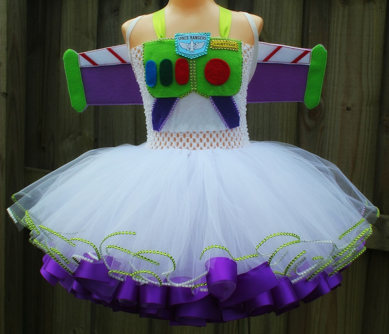 May include: White tulle tutu with purple ribbon trim and green and purple felt wings. The bodice features a green felt design with the words "Space Ranger" and "Lightyear" and a red button.