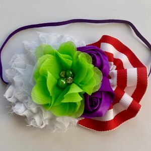May include: A purple, green, and white flower headband with a red and white striped ribbon. The headband is made of a soft, stretchy material and is perfect for adding a touch of whimsy to any outfit.