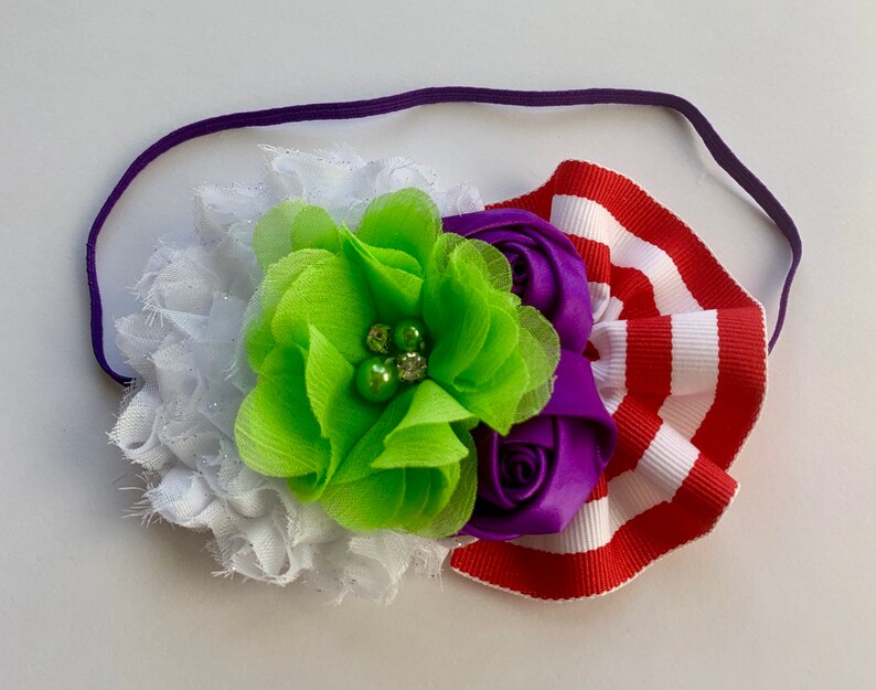 May include: A purple, green, and white flower headband with a red and white striped ribbon. The headband is made of a soft, stretchy material and is perfect for adding a touch of whimsy to any outfit.
