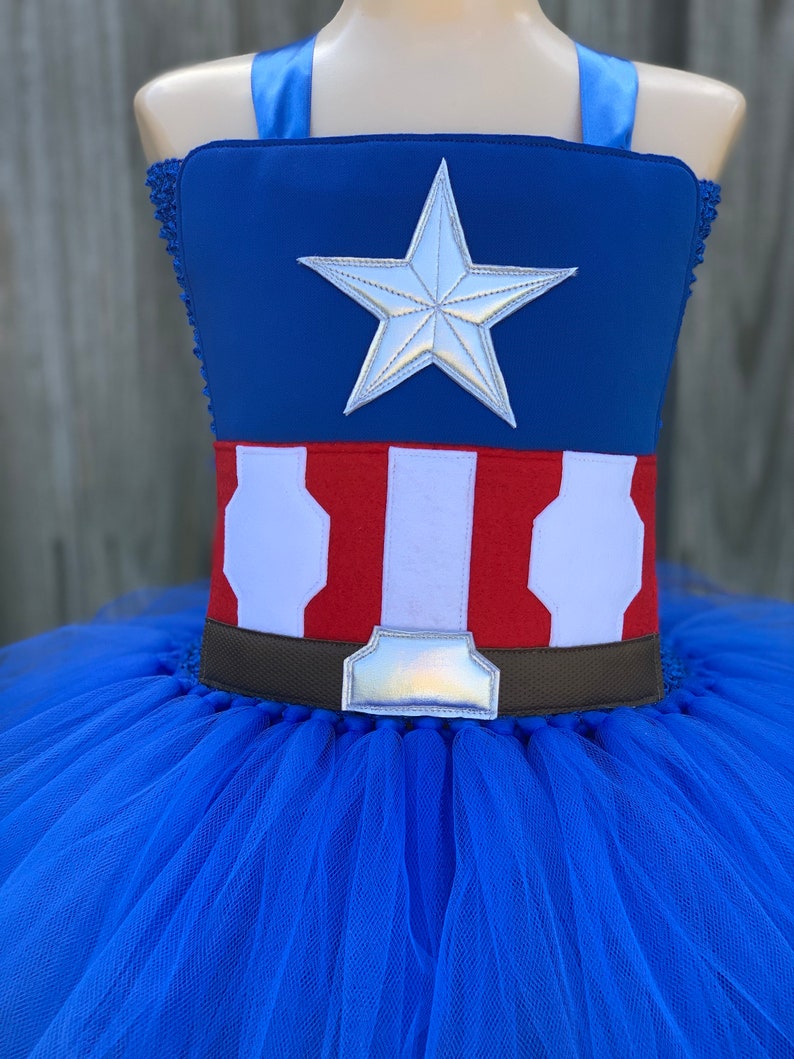 May include: A blue tulle tutu with a red, white, and blue Captain America costume top. The top features a silver star and a brown belt with a silver buckle.