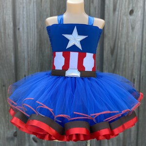 May include: A blue tulle tutu with red and brown ribbon trim. The top of the tutu is a blue and red fabric with a white star and a brown belt.