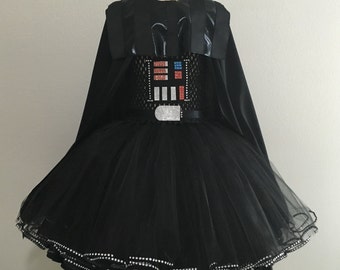 Può includere: Tutu in tulle nero con un mantello in velluto nero e un design Darth Vader in strass sul corpetto. Il tutu ha un bordo in strass argentato.