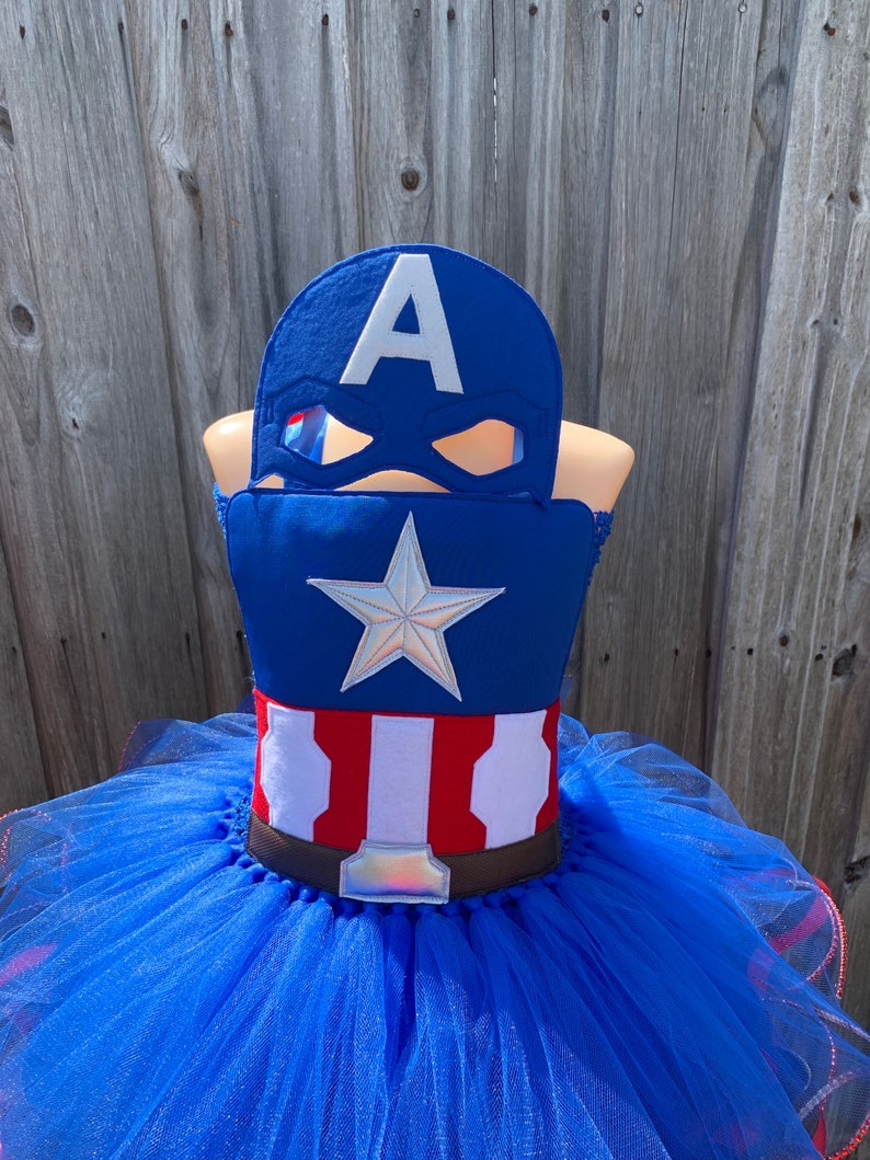 May include: A blue tulle tutu with a red, white, and blue Captain America costume top. The costume top features a white star and the letter "A" on a blue background. A brown belt with a silver buckle is included.