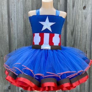 May include: A blue tulle tutu with red and brown ribbon trim. The top of the tutu is a blue and red fabric with a white star and a white and red stripe pattern.