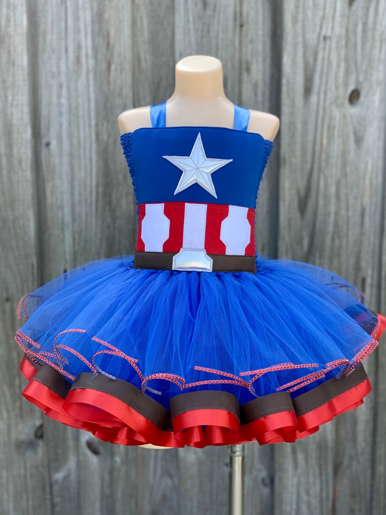 May include: A blue tulle tutu with red and brown ribbon trim. The top of the tutu is a blue and red fabric with a white star and a white and red stripe pattern.